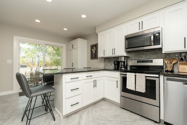kitchen featuring appliances with stainless steel finishes, a peninsula, recessed lighting, backsplash, and dark stone counters