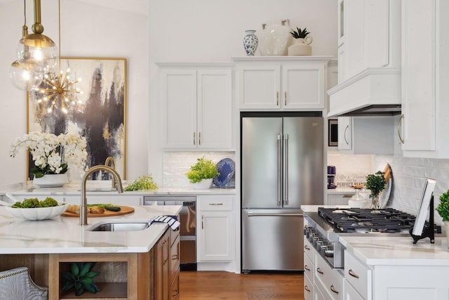kitchen with stainless steel appliances, a chandelier, backsplash, a sink, and white cabinets