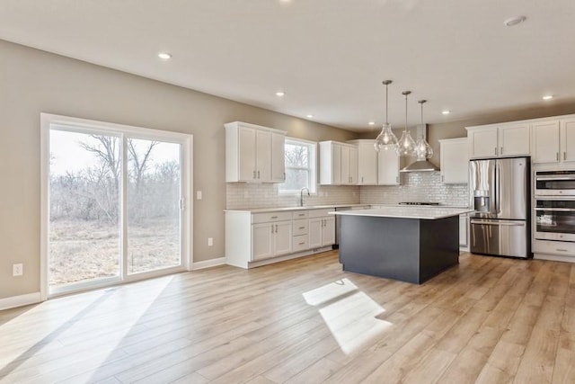 kitchen with stainless steel appliances, wall chimney range hood, a sink, light countertops, and backsplash