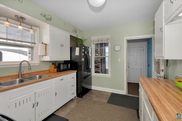 kitchen with a sink, butcher block countertops, black appliances, white cabinetry, and baseboards