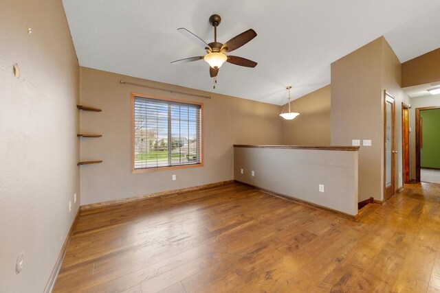 empty room with ceiling fan, wood finished floors, lofted ceiling, and baseboards