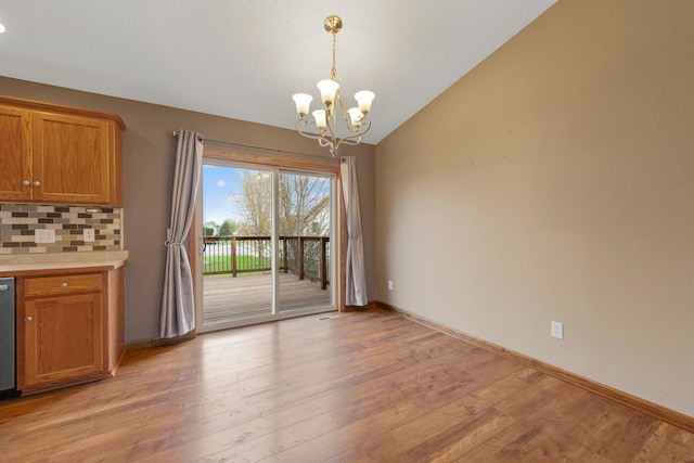 unfurnished dining area with a chandelier, vaulted ceiling, light wood-type flooring, and baseboards