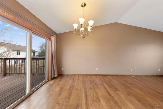 empty room featuring vaulted ceiling, a chandelier, light wood finished floors, and baseboards