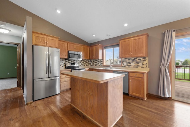 kitchen with stainless steel appliances, a center island, light countertops, wood finished floors, and lofted ceiling