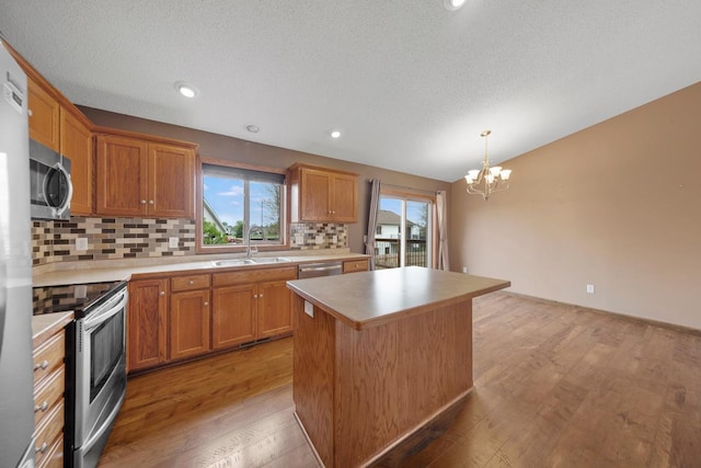 kitchen featuring appliances with stainless steel finishes, a chandelier, a kitchen island, tasteful backsplash, and light wood finished floors