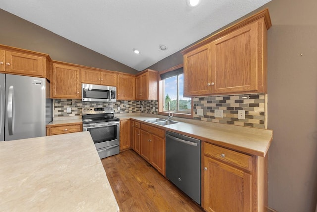 kitchen with stainless steel appliances, a sink, lofted ceiling, light countertops, and wood finished floors