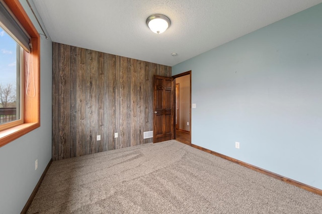 carpeted spare room with wood walls and baseboards