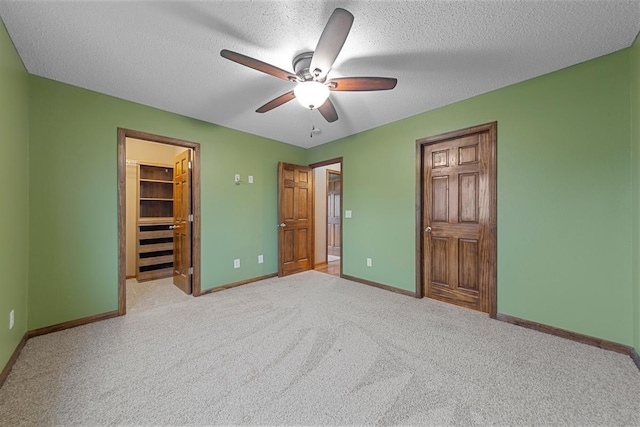 unfurnished bedroom featuring a spacious closet, a closet, baseboards, a textured ceiling, and light colored carpet
