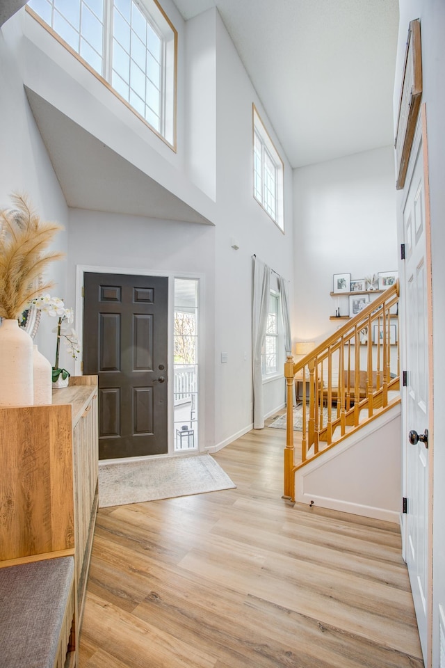 entryway featuring light wood-style flooring, a towering ceiling, stairs, healthy amount of natural light, and baseboards