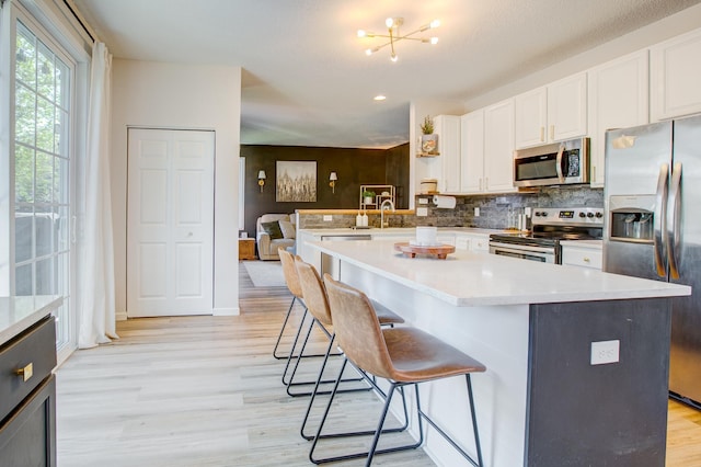 kitchen featuring appliances with stainless steel finishes, light wood-style floors, decorative backsplash, white cabinets, and a kitchen breakfast bar