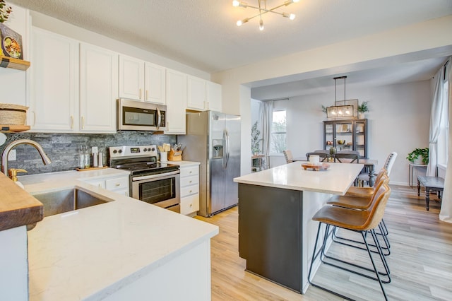 kitchen with appliances with stainless steel finishes, a sink, light countertops, white cabinets, and tasteful backsplash