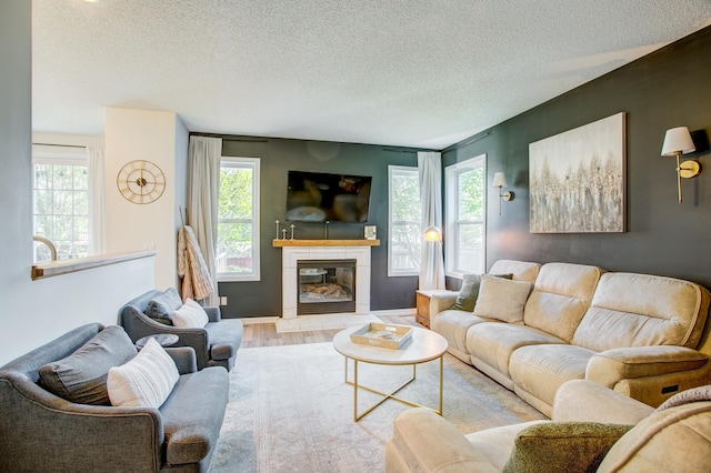 living room with wood finished floors, plenty of natural light, a textured ceiling, and a glass covered fireplace