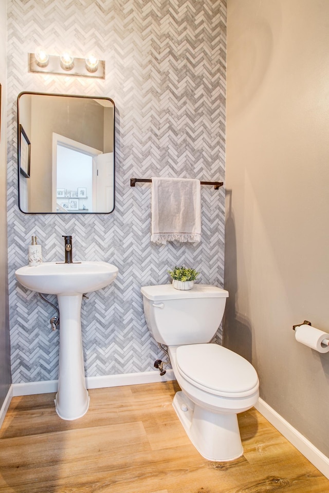 half bath with baseboards, toilet, wood finished floors, and wallpapered walls