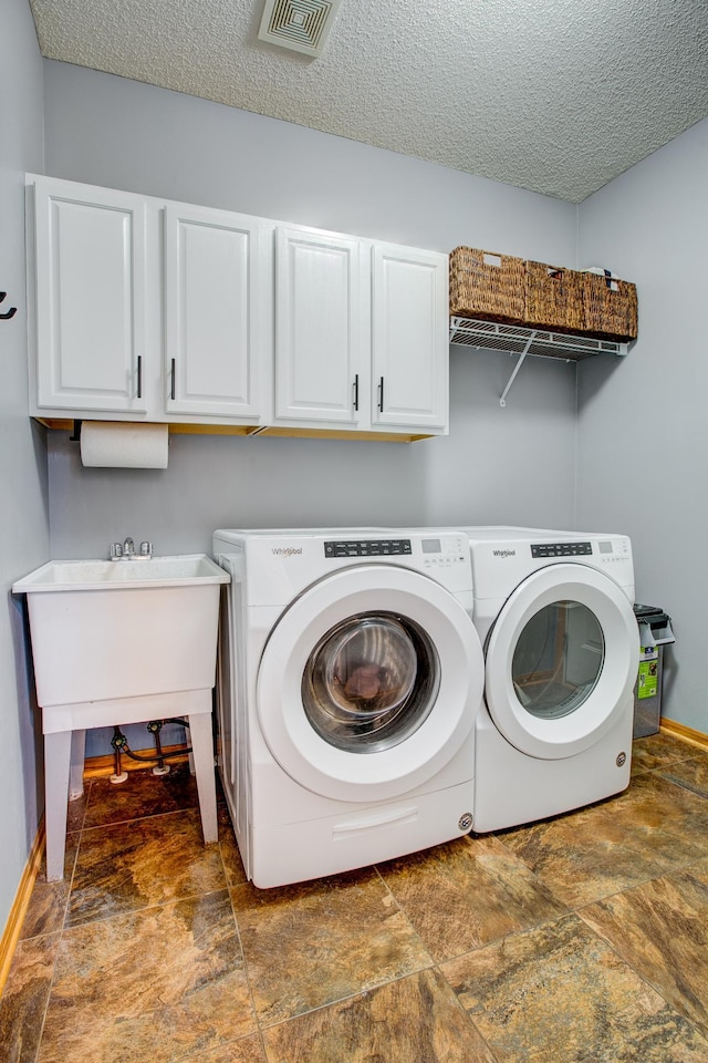 clothes washing area featuring cabinet space, stone finish floors, washer and dryer, baseboards, and a textured ceiling