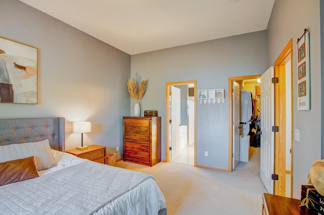 bedroom featuring a walk in closet, light carpet, ensuite bath, and baseboards