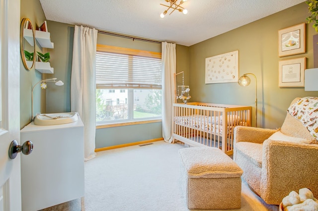 carpeted bedroom featuring a nursery area, a textured ceiling, and baseboards