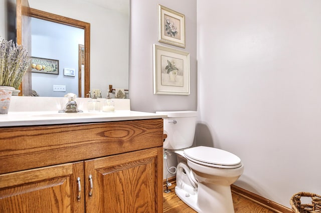 half bath with baseboards, toilet, vanity, and wood finished floors