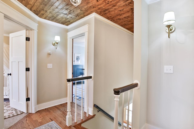 hallway featuring an upstairs landing, wooden ceiling, ornamental molding, wood finished floors, and baseboards