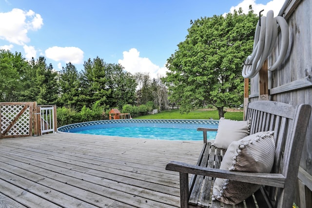 swimming pool featuring a deck, view of wooded area, and a yard
