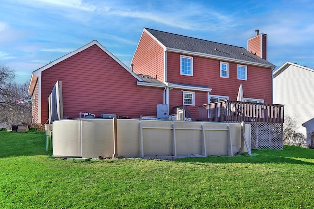 rear view of house featuring a chimney, a lawn, and a deck