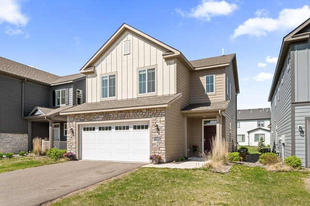 view of front of property with asphalt driveway, stone siding, a garage, board and batten siding, and a front yard
