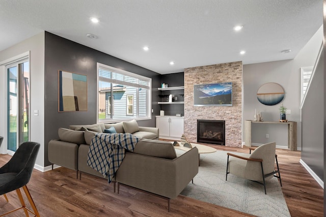 living area with wood finished floors, built in shelves, baseboards, recessed lighting, and a stone fireplace