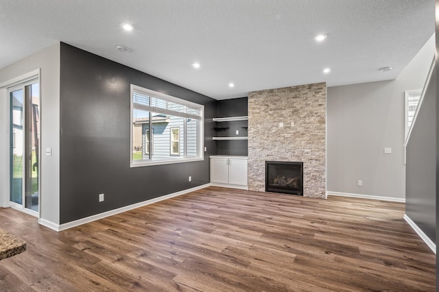 unfurnished living room featuring wood finished floors, recessed lighting, baseboards, built in features, and a stone fireplace
