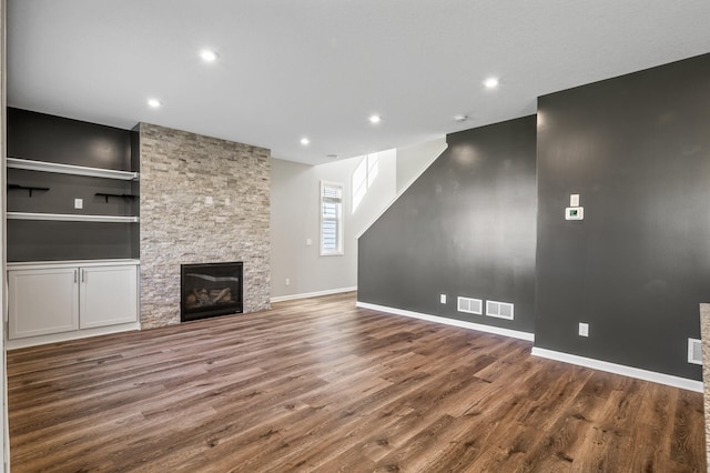 unfurnished living room featuring wood finished floors, a stone fireplace, baseboards, and recessed lighting