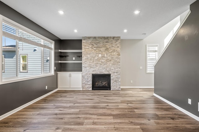 unfurnished living room featuring plenty of natural light, wood finished floors, recessed lighting, baseboards, and a stone fireplace