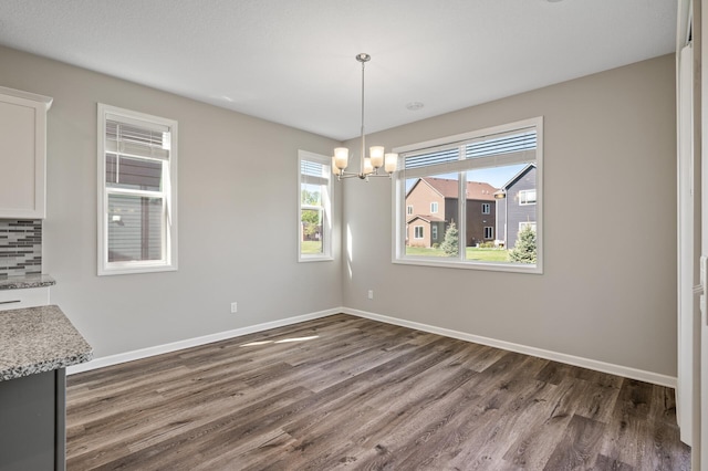 unfurnished dining area with dark wood finished floors, baseboards, and a chandelier