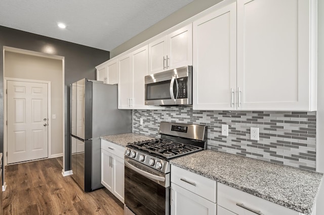 kitchen featuring stainless steel appliances, tasteful backsplash, white cabinetry, dark wood-style flooring, and light stone countertops