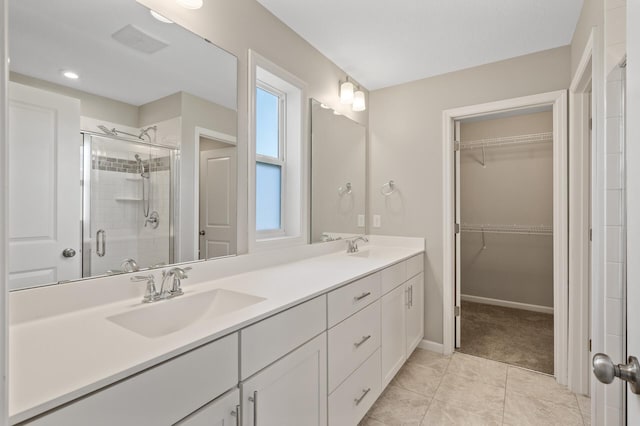 bathroom featuring a stall shower, a spacious closet, double vanity, and baseboards