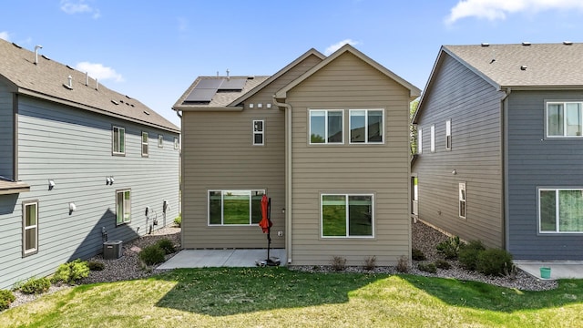back of property with a patio, central AC, a lawn, and solar panels
