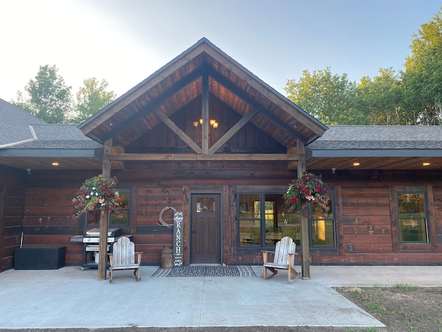 view of exterior entry featuring roof with shingles and a patio