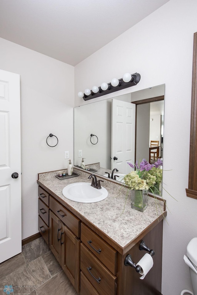 half bathroom with vanity, toilet, and baseboards