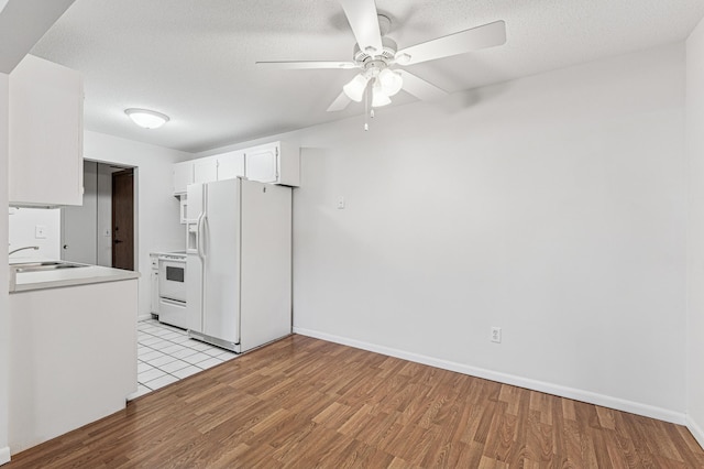 kitchen with white appliances, a sink, ceiling fan, light wood finished floors, and white cabinets