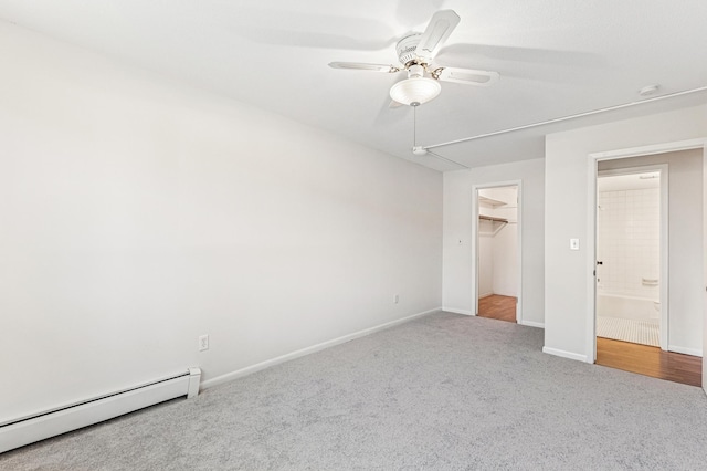 unfurnished bedroom featuring a baseboard radiator, carpet flooring, baseboards, a ceiling fan, and a walk in closet