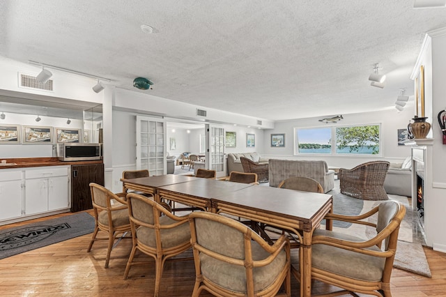 dining room with a textured ceiling, light wood finished floors, and ornamental molding