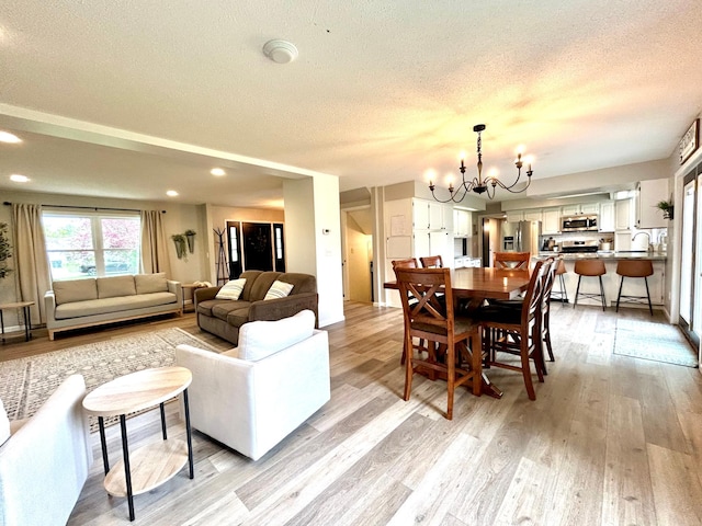 living area featuring a textured ceiling, light wood-style flooring, a chandelier, and recessed lighting