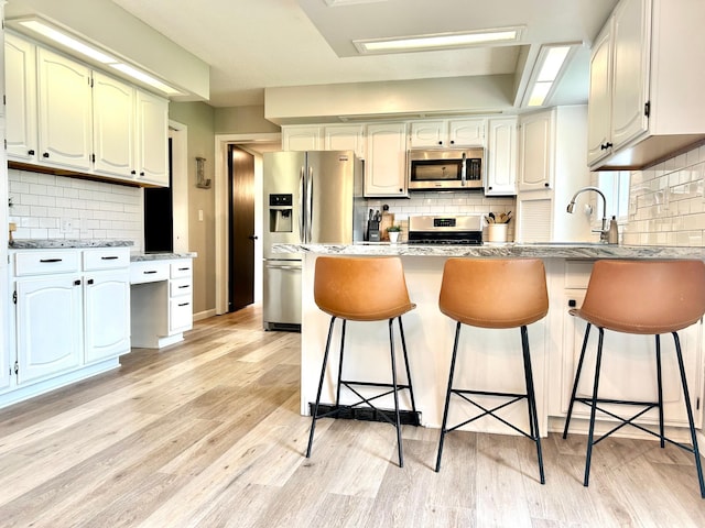 kitchen with stainless steel appliances, a peninsula, backsplash, light wood-style floors, and a sink