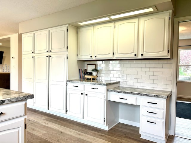 kitchen with light wood-style flooring, backsplash, light stone counters, and a textured ceiling