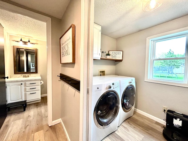 clothes washing area with washing machine and clothes dryer, cabinet space, a textured ceiling, light wood-type flooring, and baseboards