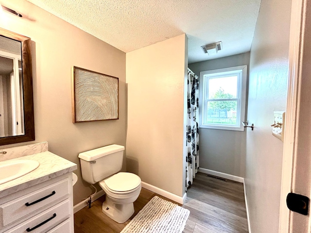 bathroom with wood finished floors, toilet, vanity, baseboards, and a textured ceiling