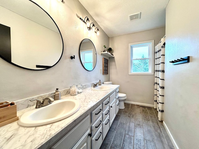 full bath with wood finished floors, toilet, baseboards, double vanity, and a textured ceiling