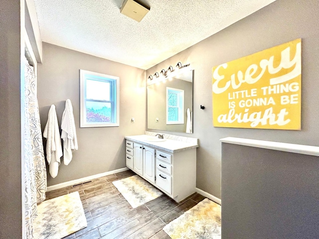 bathroom with wood finished floors, vanity, a textured ceiling, and baseboards