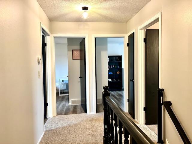 hall with an upstairs landing, a textured ceiling, carpet flooring, and baseboards