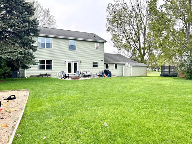 rear view of property featuring a shed, a patio, a trampoline, a yard, and an outbuilding