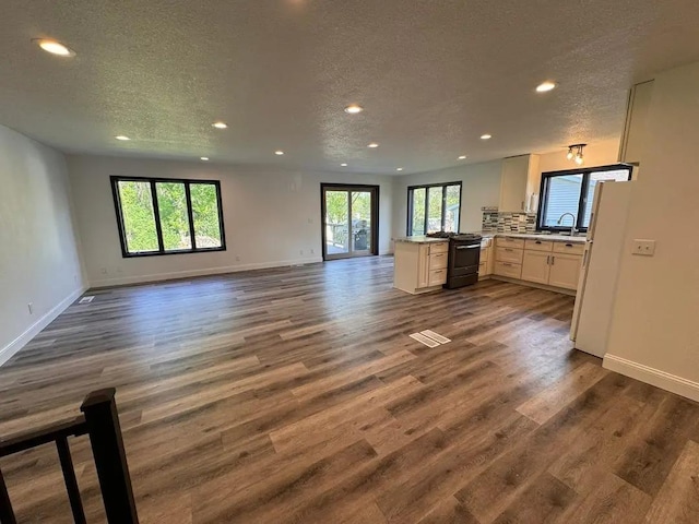 unfurnished living room with recessed lighting, a textured ceiling, dark wood-style flooring, a sink, and baseboards