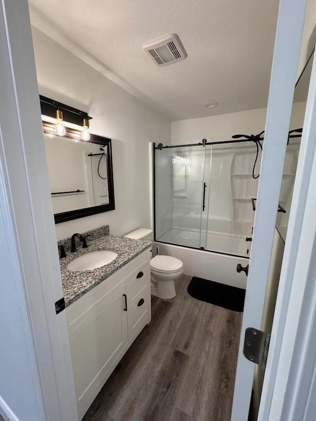 full bathroom featuring a textured ceiling, wood finished floors, vanity, bath / shower combo with glass door, and toilet