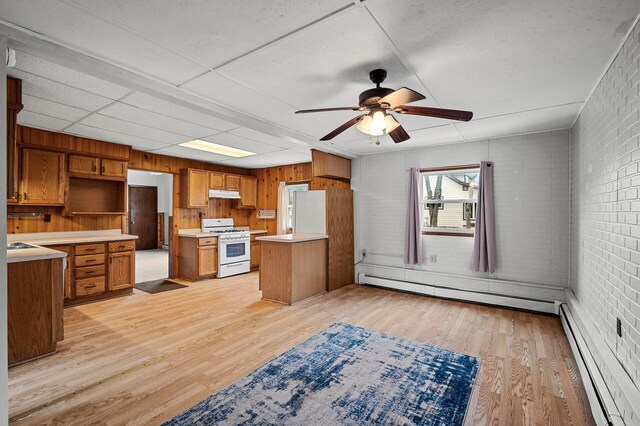 444 Vincent St, Saint Croix Falls, WI 54024 - kitchen with white gas stove, a baseboard heating unit, under cabinet range hood, brick wall, and brown cabinets